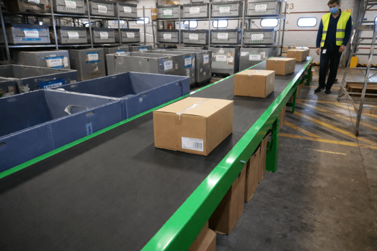 Konvejeris, skirtas dėžėms ir siuntiniams gabenti logistikos centre, su lygia gumine juosta ir lengva plienine konstrukcija.